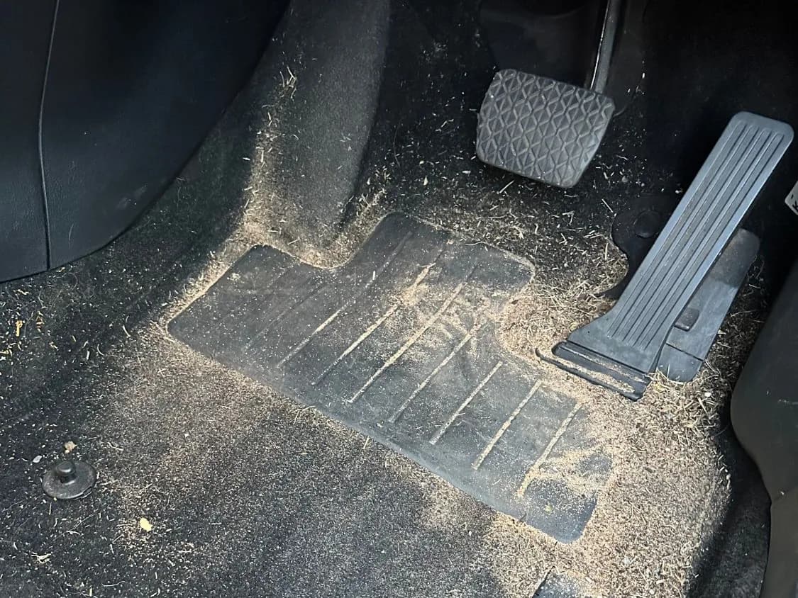 A car's driver footwell covered in sand and debris, before detailing