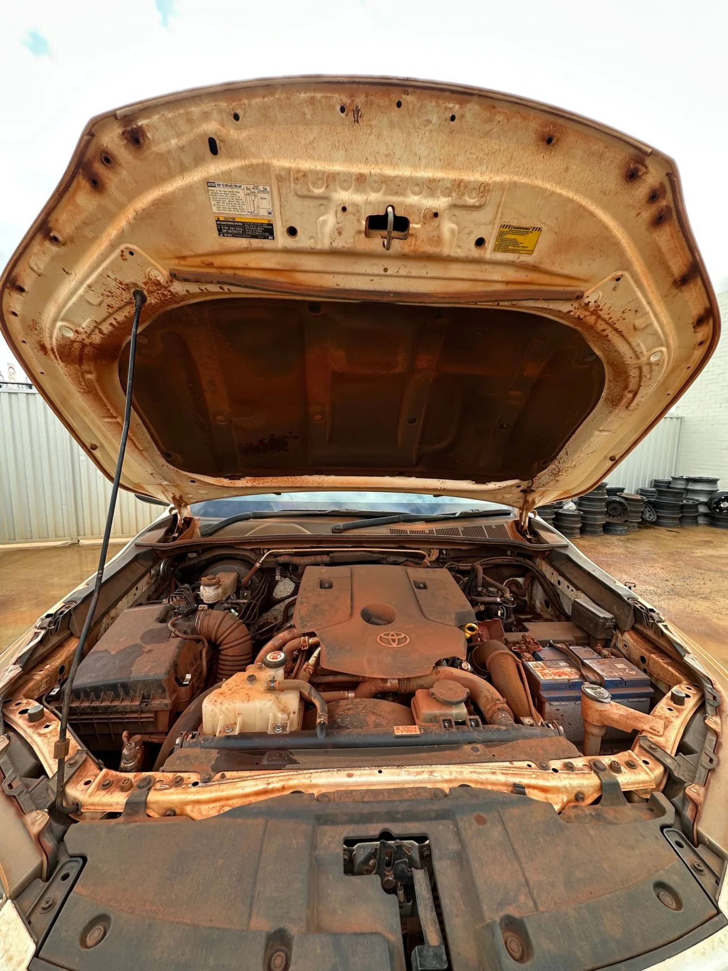 A Toyota HiLux engine bay and bonnet coated in red dust, before detailing