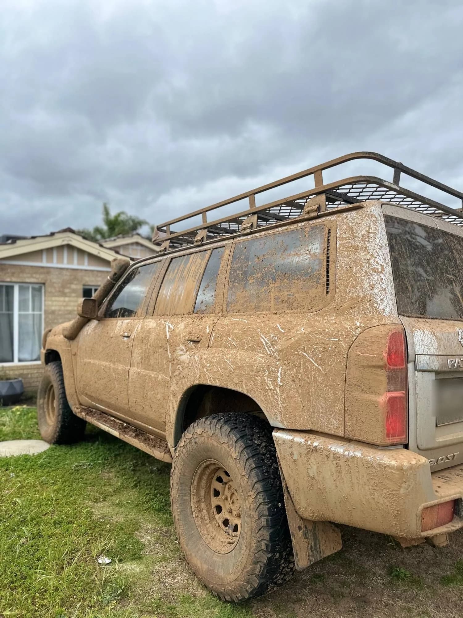 The side and rear of a Nissan Patrol caked in mud, before detailing