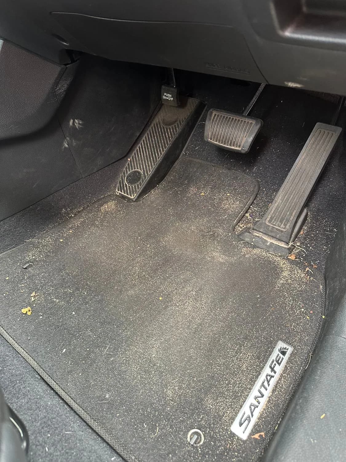 A Hyundai Santa Fe driver's footwell with dirt and debris on the mat, before detailing